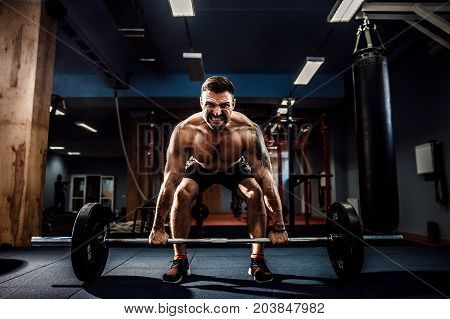 Muscular strong fitness man doing deadlift of a barbell in modern fitness center. Functional training. Snatch exercise. Scream for motivation