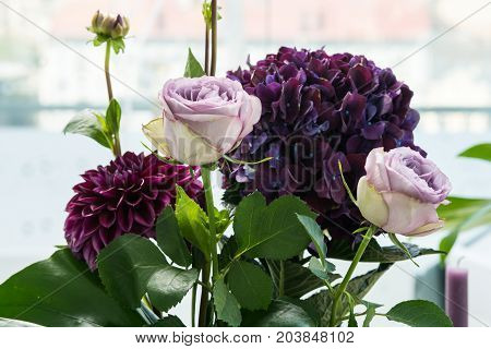 Close-up purple flowers in the vase on the table. Little bouquet made of pink roses and violet hydrangea flowers on light background. Beautiful floristic decor for event. Wedding decor