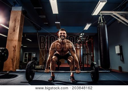 Muscular strong fitness man doing deadlift of a barbell in modern fitness center. Functional training. Snatch exercise. Scream for motivation