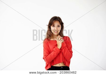 Portrait of young tender brunette teenage girl wearing red jamper looking at camera with serious or pensive expression. Caucasian woman model with medium length hair rubbing her neck posing indoors