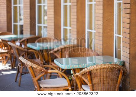 Beautiful and cosy summer terrace with light brown wicker chairs and blue tables stand opposite the windows of cafe. Shallow dof. Focus on foreground.