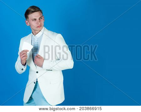 Man holding business or bank card. Businessman posing in white jacket shirt and pants. Banking and saving. Manager wearing casual suit on blue background. Fashion and information concept copy space