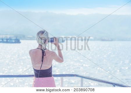 Summer travel concept - Woman taking beatiful sea photo with smartphone camera in blue sky background Indonesia