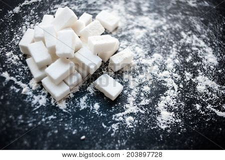 Unhealthy food concept - sugar and flour on a black background. Dangerous high amount of sugar in food. Carbohydrates sources top view