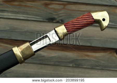 hilt and part of the sword blade half pushed out of the sheath close-up against a blurred wooden wall