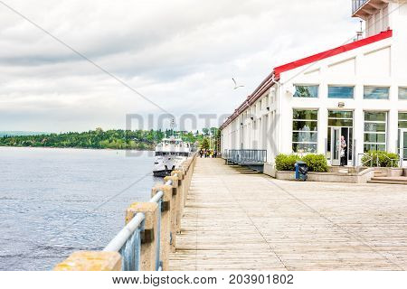 Saguenay Canada - June 3 2017: Sidewalk terrace boardwalk in downtown city park in Quebec during summer with river and tour boat and people walking