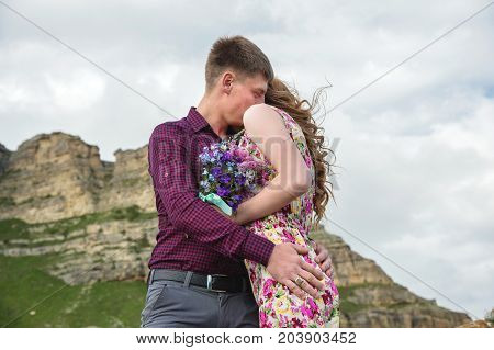 View from the back. Young couple hugging kisses against the blue sky and rocks. The concept of ideal relations and family