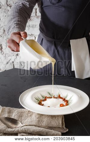 Waiter pouring broth to mushroom cream soup. Original restaurant serving of delicacy meal, copy space