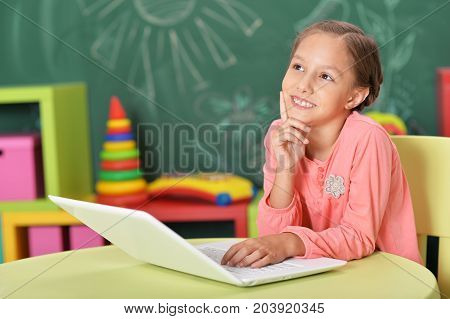 Cute little girl sitting at table and using laptop