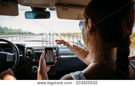 Girl uses navigator in smartphone in the car, sitting on passenger seat, traveling with help of modern gps navigation system