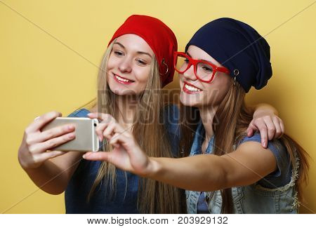 lifestyle, tehnology and people concept: Happy girls  with smartphone  over yellow background. Happy selfie.