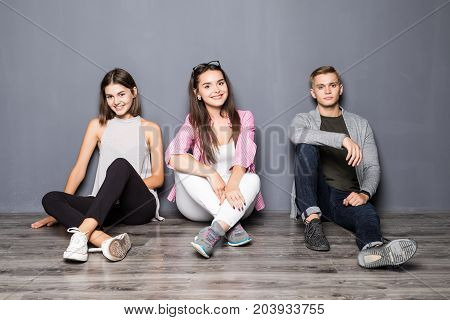 Group Of Friends Sitting On Floor On Gray Background