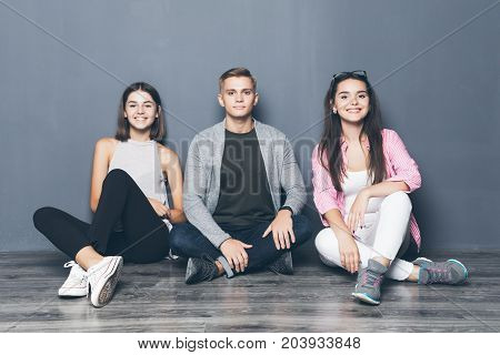 Group Of Friends Sitting On Floor On Gray Background