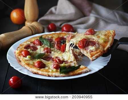 Hot pizza slice with melting cheese on a dark wooden table with tomatos.Gray drape.