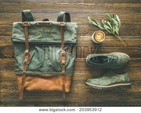 Flat-lay of woman's fall accessories and coffee. Haki suede leather oxford boots, large green backpack and cup of espresso over wooden background, top view