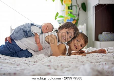 Two Children, Toddler And His Big Brother, Hugging And Kissing Their Newborn Baby Brother