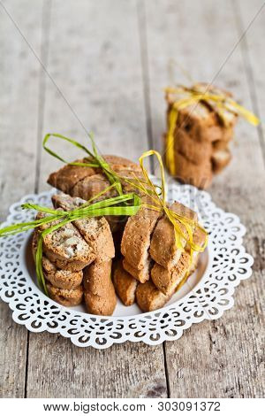 Fresh homemade Italian cookies cantuccini stacked on white plate on ructic wooden table background. Sweet food with copy space.