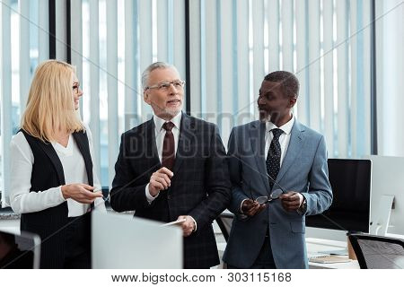 Happy Blonde Woman Looking At Businessman In Glasses Near Afrian American Man
