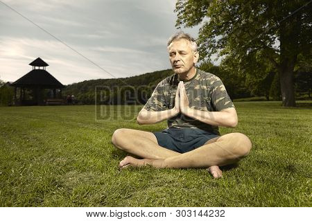 Older Man Practicing Meditation Rituals In Summer City Park
