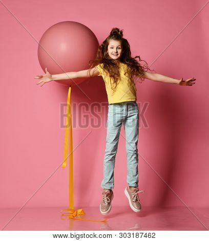 Smiling Young Teen Girl In Blue Jeans And Yellow T-shirt With Her Hands Spread Levitates The Same As