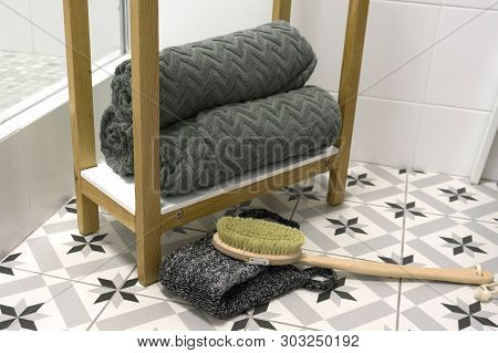 Gray Beautifully Folded Towels On A White Shelf With A Massage Brush And Washcloth.