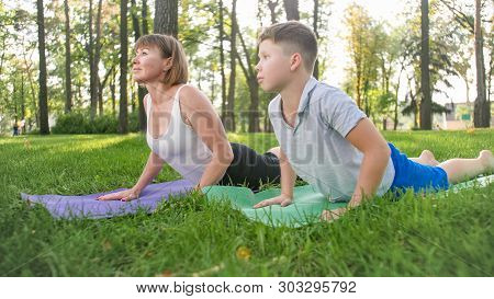 Photo Of Middle Aged Woman Teaching Her Student In Yoga Class At Park. Woamn With Teenage Boy Practi