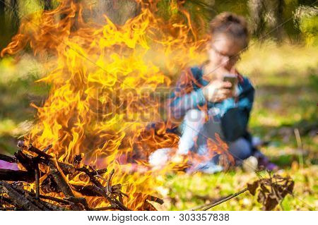 The Girl With The Phone Is Unobtrusively Visible By Fire And Smoke From The Bonfire In The Autumn In