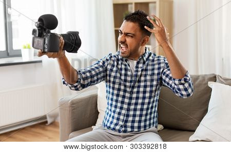 blogging, videoblog and people concept - angry indian male video blogger with camera videoblogging at home