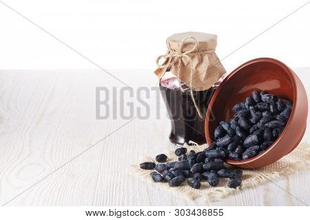 Honeysuckle berries in a ceramic bowl  and glass jar of jam stand  on a wooden table on white background.