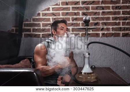 Brutal Guy Is Blowing Smoke In The Shisha Hose.