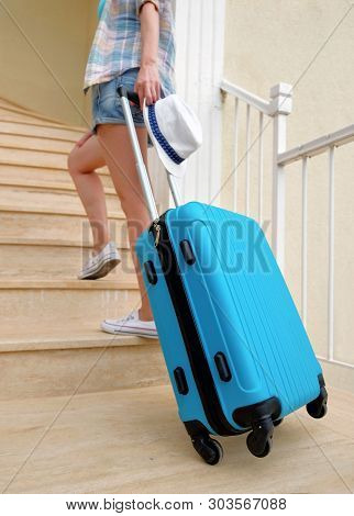 A Young Travel Woman In White Sneakers Carries A Blue Suitcase Up The Stairs To The Hotel
