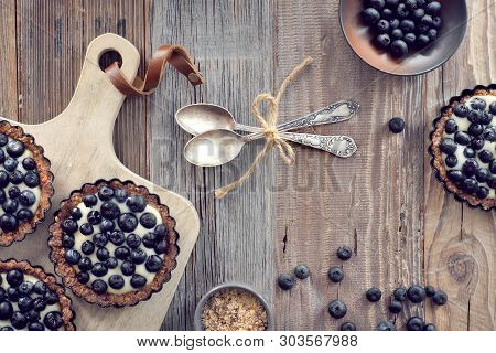 Top View On Wholegrain Blueberry Tarts With Vanilla Cream On Rustic Wooden Background