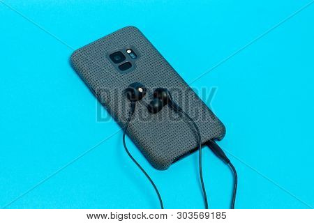 Smartphone In Stylish Textile Case With Connected Headphones On Blue Background