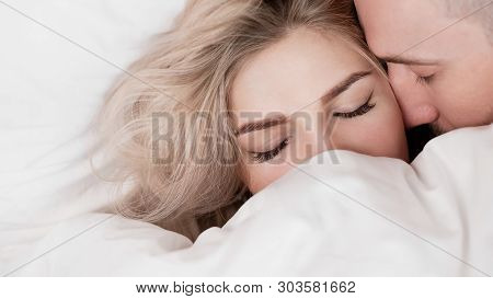 Married Couple, Man And Woman, Are Lying In Bed, Hugging And Sleeping On White Bedding. Hiding Their