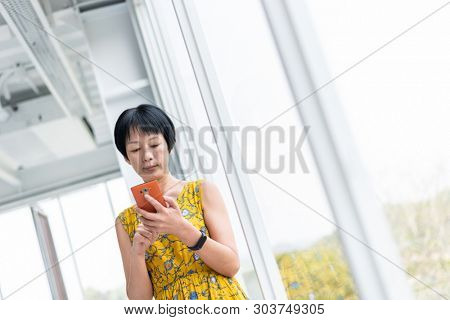 mature Asian woman using cellphone at a modern building