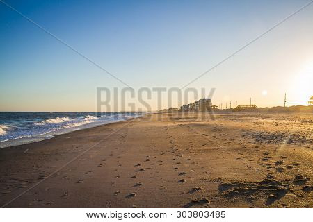 Foot Prints In The Sand Leading Away Form The Viewer On A Long Sandy Beach In Evening Light.