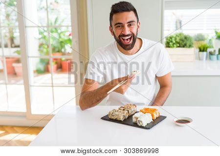 Handsome man smiling happy enjoying eating fresh colorful asian sushi using chopsticks