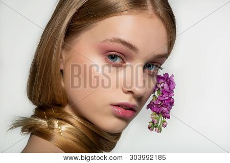 Close Up Portrait Of Young Girl With Blue Eyes, Bright Makeup, Neck Wrapped In Hair, Purple Flowers 