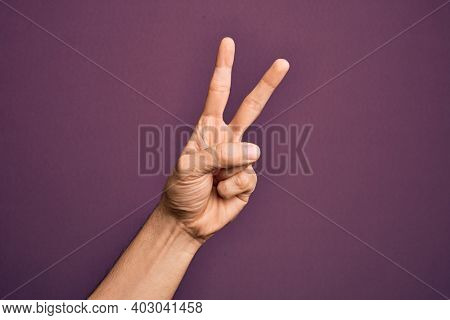 Hand of caucasian young man showing fingers over isolated purple background counting number 2 showing two fingers, gesturing victory and winner symbol