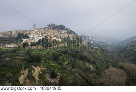 Foggy morning at the hill of Polop de Marina with church and castell over green forest at the Costa Blanca, Spain