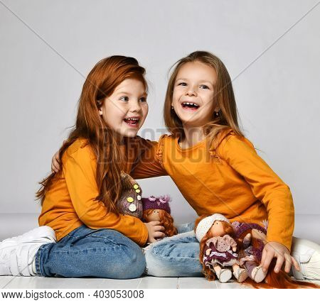 Two Frolic Laughing Kid Girls Friends In Similar Clothes Sit On Floor In Kindergarten Playing With T