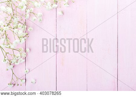 Floral frame of small  white flowers ( Gypsophila)  on light pink wooden background. Vintage style image. Flat lay