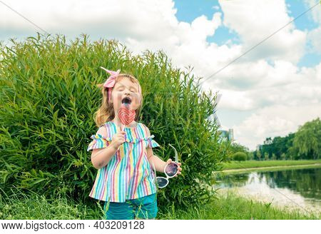 Fashionable Baby Girl, Sunglasses, Lollipop Like A Heart.little Three Year Old Girl Licks A Colored 