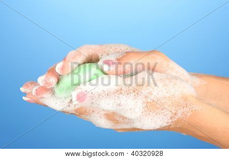 ผู้หญิงมือใน soapsuds บนพื้นหลังสีฟ้าอย่างใกล้ชิด