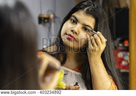 A Beautiful Indian Woman In White Saree Applying Eye Liner In Front Of Mirror With Smiling Face