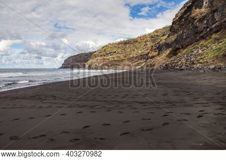 Empty Wild Beach With Foot Steps On Black Sand. Rocks And Ocean On Tenerife, Spain