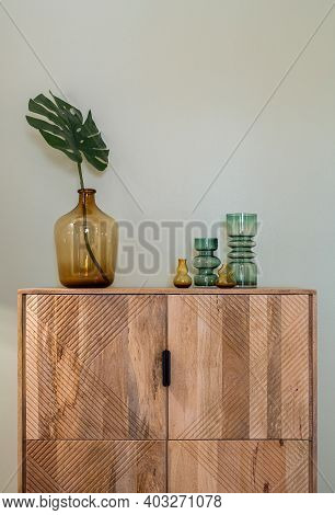 Transparent Colorful Vases For Flowers And Big Bottle With Monstera Leaf On Wooden Cupboard. Decorat