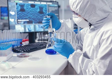 Man In Microbiology Lab Holding Petri Dish Working With Micropipette Wearing Coverall. Chemist In Mo