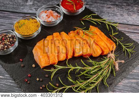 Chicken Fillet Thinly Sliced On A Black Ceramic Plate With Cooking Spices, Chili And Rosemary. Raw M