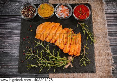 Chicken Fillet Thinly Sliced On A Black Ceramic Plate With Cooking Spices, Chili And Rosemary. Raw M